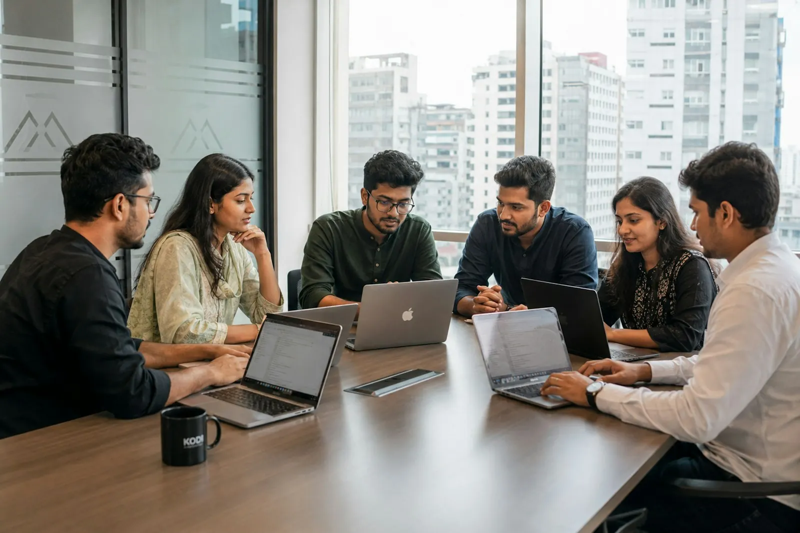 Six colleagues working together around a conference table with laptops
